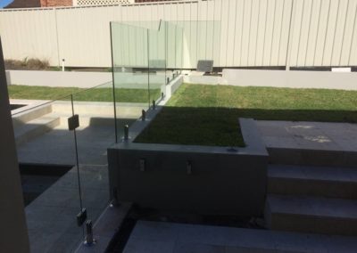 Frameless glass panel mounted to the side of a concrete wall with side mount spigots, preventing the wall from being a foothold.