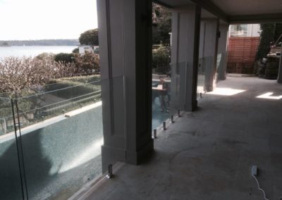 Elegant patio area featuring frameless glass pool fencing with the backdrop of a serene harbour view.