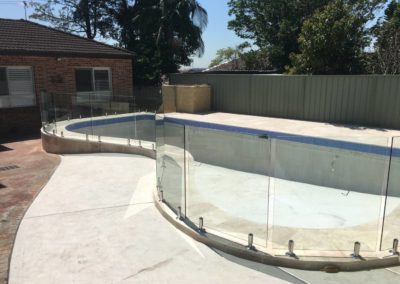 Kidney shaped pool bordered by staggered straight frameless glass panels in varying sizes, installed to follow the pool's contours.