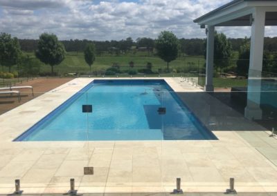 Spacious pool with frameless glass fencing and stainless steel spigots, overlooking a scenic countryside.