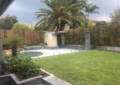 Backyard with DIY pool fencing featuring glass panels, Polaris hinges, and stainless steel spigots amidst lush greenery.