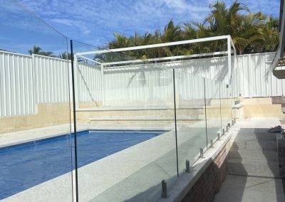 Frameless glass pool fence supplied for DIY installation by customer, showcasing a clear safety barrier around a serene pool area with tropical palm trees in the background, enhancing outdoor Australian living.